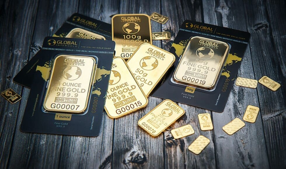 Various gold bars and gold coins displayed on a dark surface.