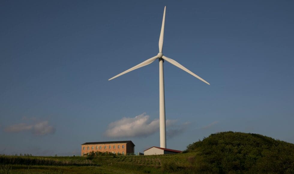 A wind turbine stands tall against a clear blue sky above a small building.
