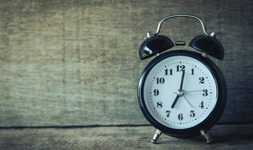 A classic black alarm clock shows the time as 6:15 on a wooden surface.